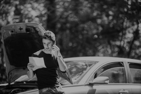 young man looking at car insurance policy while sitting next to damaged car